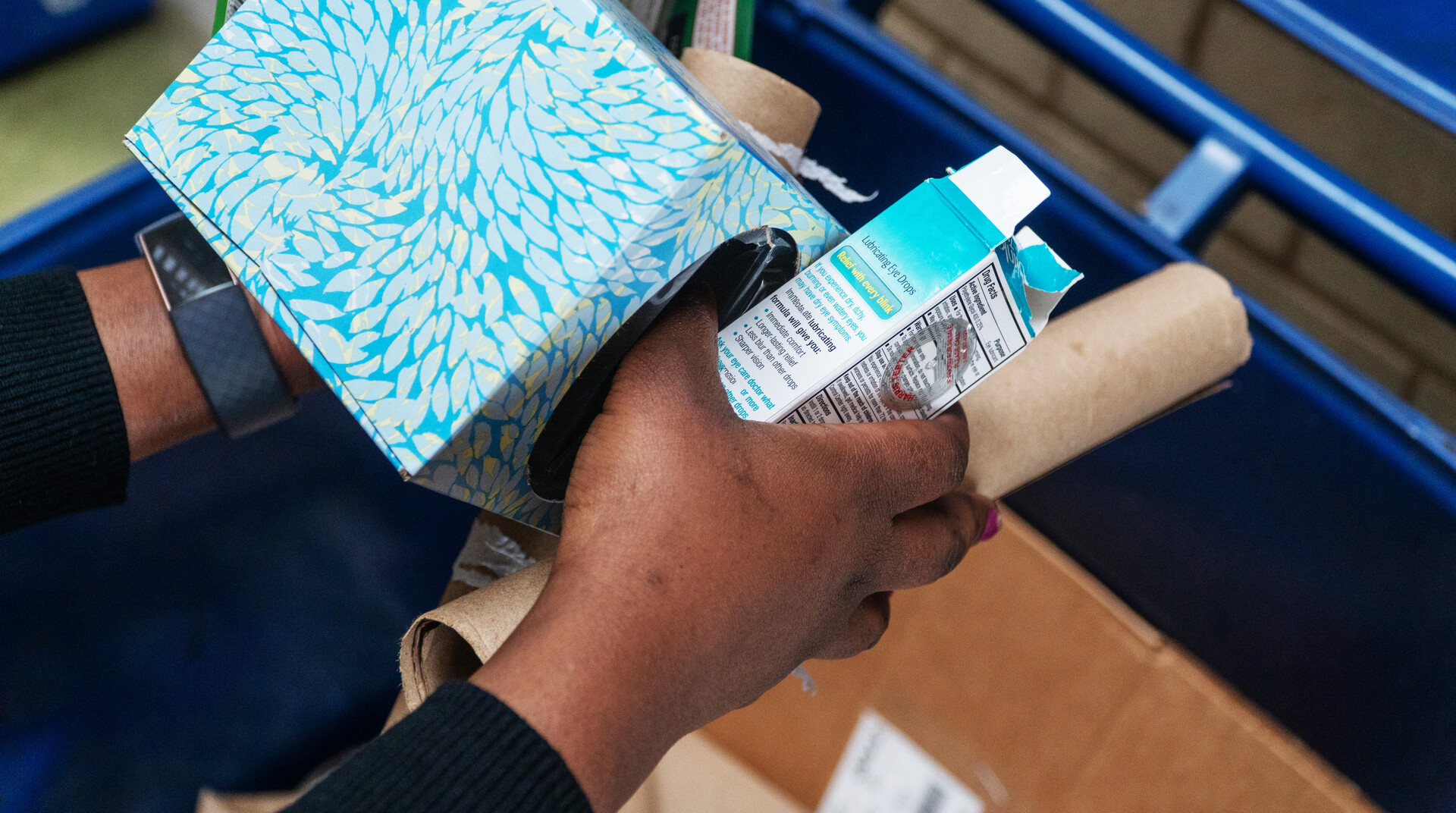 A person putting paper and cardboard items into a recycling bin.